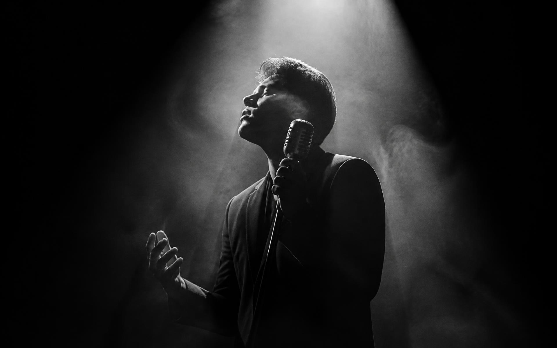 Singer performing under a spotlight on a dark stage